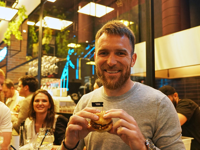 A guest of the SMASHER&CO restaurant is holding a Supreme Bacon burger in his hands